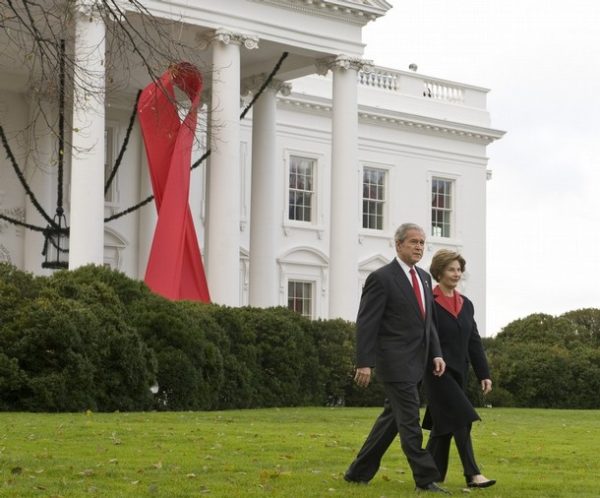 WASHINGTON - DECEMBER 1: (AFP OUT) U.S. President George W. Bush (L), accompanied by first lady Laura Bush, walks in front of a large red ribbon to deliver remarks on World Aids Day on the North Lawn of the White House December 1, 2008 in Washington, DC. President Bush was to announce that his administration had already achieved its objective of providing funding for treatment for two million people with HIV/AIDS by the end of 2008. (Photo by Mannie Garcia-Pool/Getty Images)