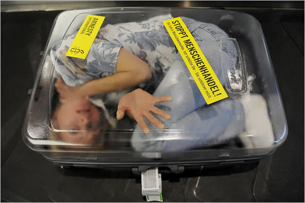 Oliver Lang/Agence France-Presse — Getty Images. Munich. December 2008. A woman demonstrated against human trafficking on a luggage belt at the airport in Munich. Amnesty International staged the protest to commemorate the 60th anniversary of the Universal Declaration of Human Rights by the United Nations.