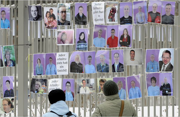 (image: Norbert Millauer/Agence France-Presse — Getty Images. caption: Two women looked at portraits of employees of the bankrupt German memory chip maker Qimonda fixed on a fence at the company's plant in Dresden, in eastern Germany, (The text near the portraits reads "Every workplace has a face.") Qimonda said a week ago that it will slash production and have to find a buyer by the end of March 2009 or else be forced to shut down