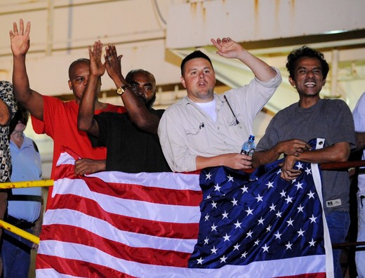 Crew members of the US merchant ship Maersk Alabama gather around a US flag while celebrating that the captain of their ship, Richard Phillips,  which had been held captive by the pirates had been freed on April 12, 2009. Somali pirates tried to seize the ship early on April 8, while it was in the Indian Ocean about 500 kilometres (310 miles) off the Somali coast.  CNN television, citing a senior US official, reported that three of the four pirates holding Phillips had been killed, and the fourth pirate was in custody.     AFP PHOTO/Roberto SCHMIDT (Photo credit should read ROBERTO SCHMIDT/AFP/Getty Images)