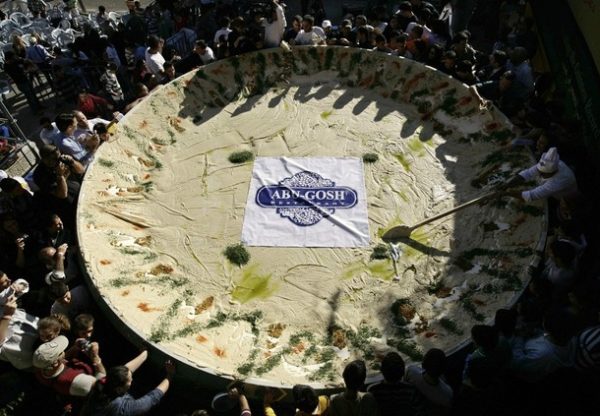 People stand around a large dish filled with hummus in Abu Gosh