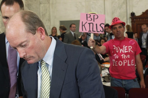 A protester holds a sign behind McKay, President of BP America, during a break in testifying before a senate hearing in Washington