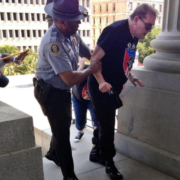 In this photo provided by Rob Godfrey, police officer Leroy Smith, left, helps a man wearing National Socialist Movement attire up the stairs during a rally Saturday, July 18, 2015, in Columbia, S.C. Members of the group were protesting Saturday the removal of the Confederate flag from the Statehouse grounds earlier this month. (Rob Godfrey via AP)