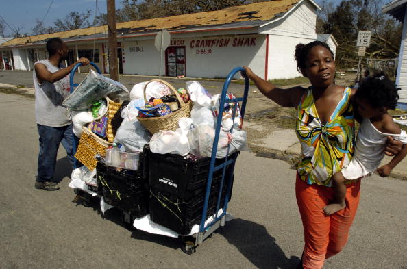 Monica Moore (R), daughter Diamond and Darrell Dillworth (L) push belongings they could salvage from their home in the Point Cadet neighborhood, 30 August, 2005, after being hit by Hurricane Katrina in Biloxi, Mississippi.AFP PHOTO/Stan HONDA (Photo credit should read STAN HONDA/AFP/Getty Images)
