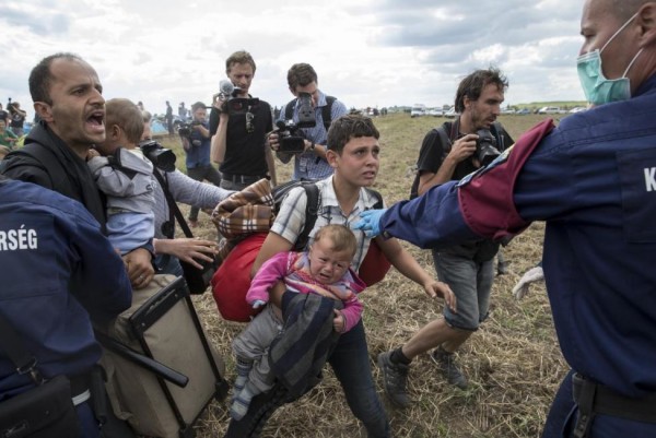 A migrant carrying a baby is stopped by Hungarian police officers as he tries to escape on a field nearby a collection point in the village of Roszke