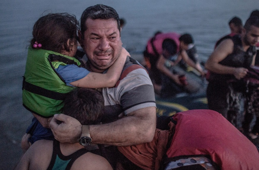 Daniel Etter for The New York Times. caption: Human face of a tragedy: A Syrian refugee from Deir Ezzor, holding his son and daughter in a life jacket, broke out in tears of joy last week after arriving on the shore of the Greek island of Kos using a flimsy inflatable boat crammed with about 15 men, women and children. 