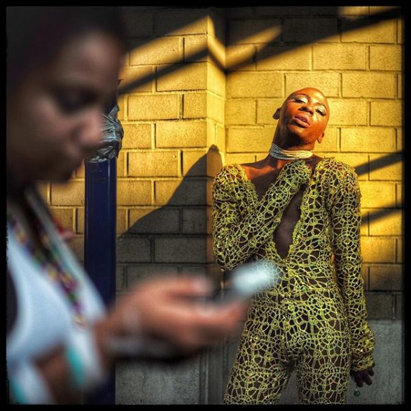 A woman looking at her phone and man in a yellow outfit at the New York City gay pride parade, 2016. Instagram photo by Ruddy Roye.
