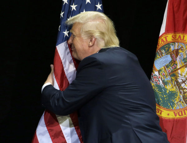 Republican presidential candidate Donald Trump pauses during his campaign speech to hug the American flag Saturday, June 11, 2016, in Tampa, Fla. (AP Photo/Chris O'Meara)
