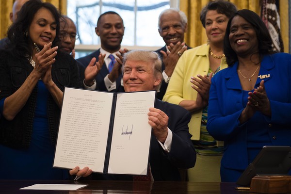 Donald Trump (C) holds up an executive order to bolster historically black colleges and universities (HBCUs) after signing it in the Oval Office of the White House in Washington, DC, February 28, 2017. / AFP / JIM WATSON