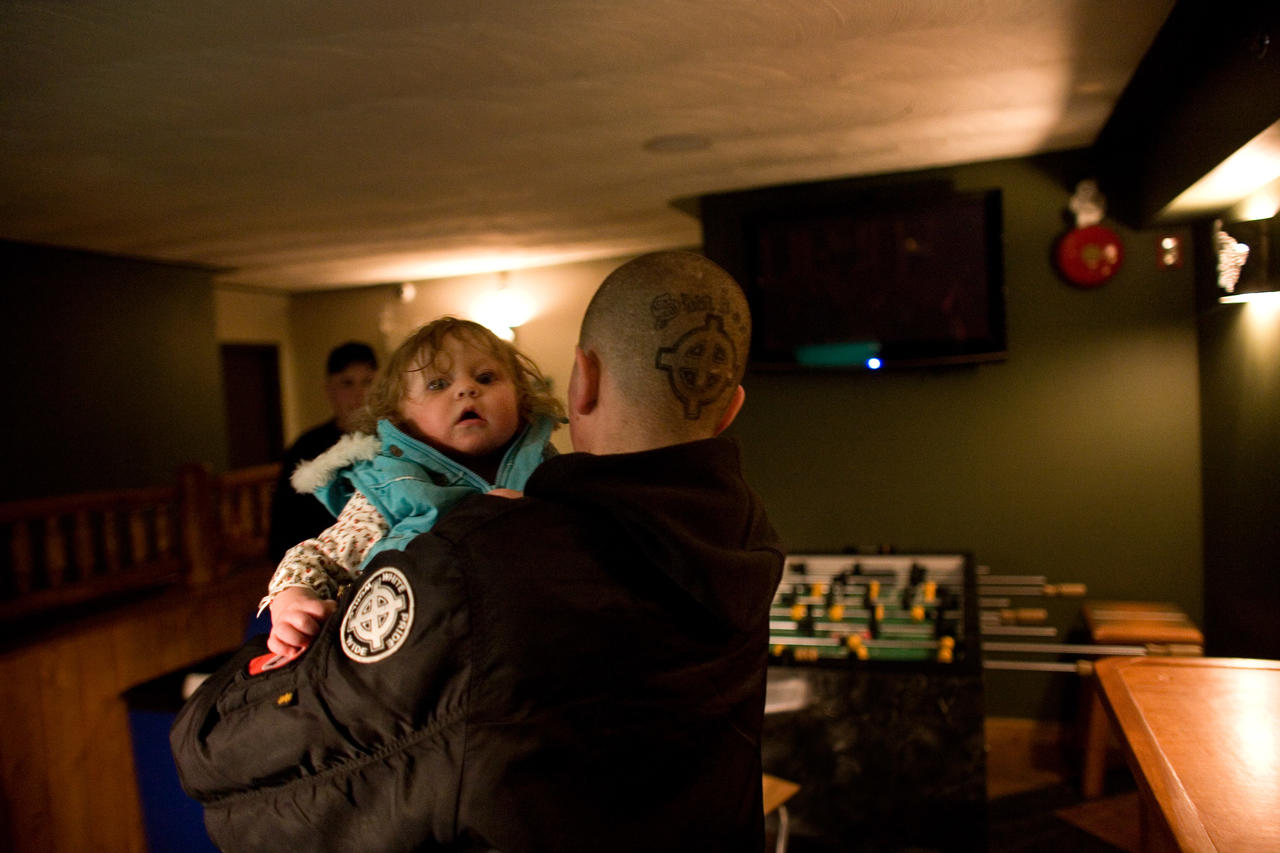 Aryana is carried by Conor, March, 2009. Canmore, Canada. Conor carries another skinhead’s daughter. The young girl’s parents were both members of the Neo-Nazi group. Photo: Brett Gundlock
