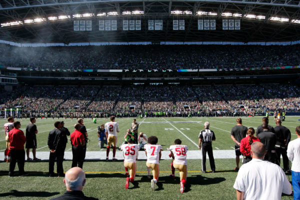 Joe Nicholson / USAToday Sports via Reuters Caption: From left, safety Eric Reid, Kaepernick and linebacker Eli Harold knelt during the national anthem before an N.F.L. game against the Seahawks last September.