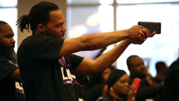 An attendee holds a cell phone like a gun during a special city council meeting at Sacramento City Hall on March 27, 2018 in Sacramento, California. Hundreds packed a special city council at Sacramento City Hall to address concerns over the shooting death of Stephon Clark by Sacramento police. (Photo by Justin Sullivan/Getty Images)