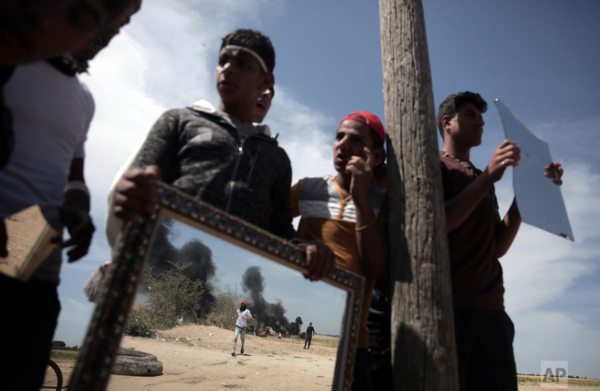 PHOTO: Khalil Hamra/AP CAPTION: Palestinian protestors are seen through mirrors used to reflect the sun light at Israeli soldiers during a protest next to the Gaza Strip border with Israel, east of Khan Younis, Monday, April 2, 2018.