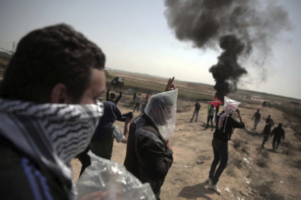 Palestinian protesters wear plastic bags on their heads as a protection from the teargas fired by Israeli troops during a protest at the Gaza Strip’s border with Israel, Friday, April 6, 2018. (AP Photo/ Khalil Hamra)