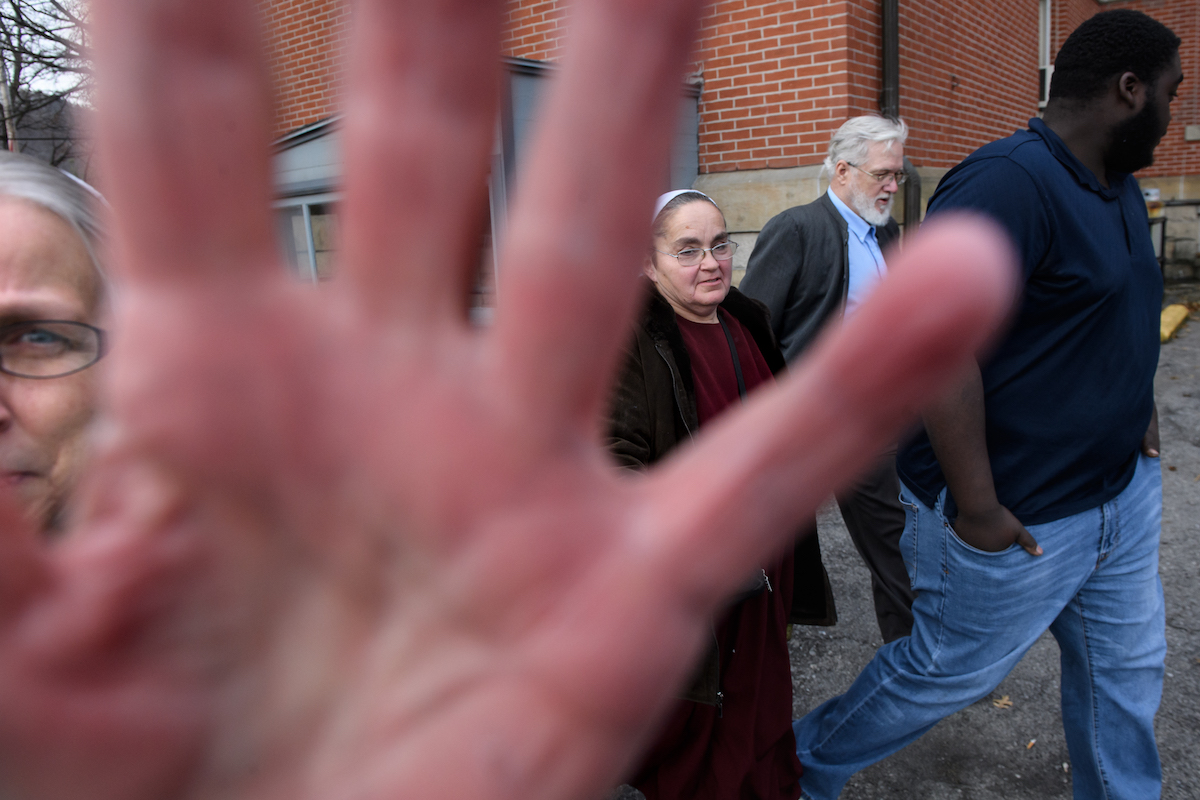 Maryann Fisher, left, of Alexandria, blocks the photographer’s camera as her husband, former pastor David Fisher, second from right, 64, leaves the Huntingdon County Courthouse after pleading no contest to a felony charge of endangering the welfare of a child in failure to report sexual abuse on Thursday, Jan. 10, 2019, in Huntingdon. Echoes of abuse coverups ring throughout Plain churches across the country in a culture that has historically emphasized a separation from the outside world. With them are the wife of Daniel R. Hostetler, Katie Hostetler, second from left, and Fisher’s adopted son, Charlie Fisher, far right. (Stephanie Strasburg/Post-Gazette) 