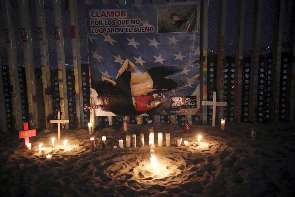 Candles are placed next to the border fence that separates Mexico from the United States, in memory of migrants who have died during their journey toward the U.S., in Tijuana, Mexico, late Saturday, June 29, 2019. On the border fence hangs a cartoon depiction of a news photograph of the bodies of Salvadoran migrant Óscar Alberto Martínez Ramírez and his daughter Valeria, who drowned on Sunday, June 23 on the banks of the Rio Grande between Matamoros, Mexico, and Brownsville, Texas. Photo: Emilio Espejel, AP