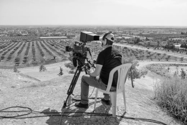 Photo: Emin Ozmen / Magnum Photos. A TV reporter broadcasts on a hill in the border town of Ceylanpinar, as Turkish military fights with Kurdish rebels in Ras al-Ayn in northern Syria.
