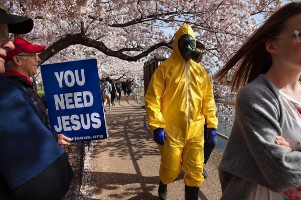 Photo: Jacquelyn Martin/AP. Caption: A 17-year-old who asked not to be named wears a yellow hazmat suit, gas mask, boots, and gloves as he walks with his family, from Gaithersburg, Md., under cherry blossom trees in full bloom along the tidal basin, Sunday, March 22, 2020, in Washington. "I'm not worried for me since I'm young," says the 17-year-old, "I'm wearing this in case I come into contact with anyone who is older so that I won't be a threat to them." He plans to wear his protective outfit for coronavirus each time he leaves the house. Sections of the National Mall and tidal basin areas have been closed to vehicular traffic to encourage people to practice social distancing and not visit Washington's iconic cherry blossoms this year due to coronavirus concerns. The trees are in full bloom this week and would traditionally draw a large crowd.