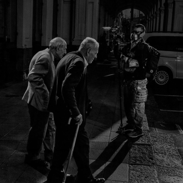 Two old friends at the Catania train depot pass a TV cameraman. On the eve of the nationwide lockdown, the last train bearing passengers from northern Italy is three hours late. Phot by Alex Majoli/Magnum Photos