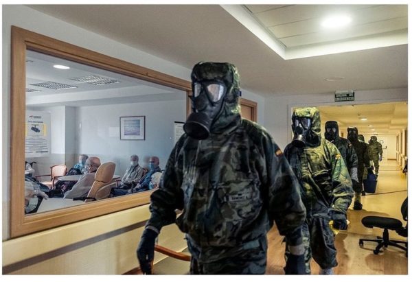 Photo: Carlos Spottorno/Panos Pictures. Caption: Residents in a nursing home sit together in a common room as members of the NBC (Nuclear, Biological and Chemical) company of the paratrooper brigade arrive to carry out decontamination tasks at the facility. Alcala de Henares, Spain, 2020.⠀
