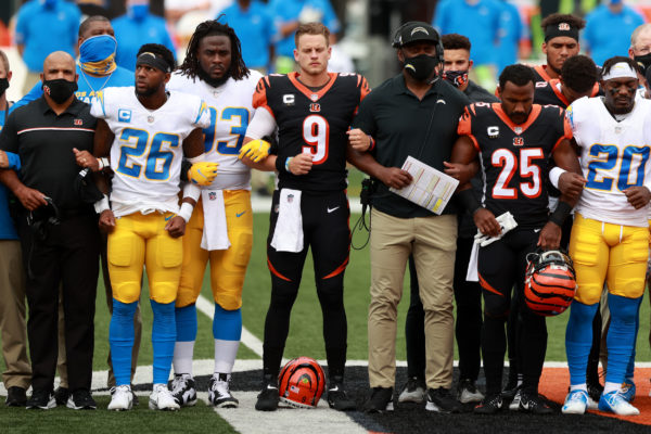 Photo: Bobby Ellis/Getty Images. Quarterback Joe Burrow #9 of the Cincinnati Bengals, teammates and the Los Angeles Chargers stand in unity during the U.S. National Anthem at Paul Brown Stadium on September 13, 2020 in Cincinnati, Ohio. The NFL began their 2020 season and the Bengals didn't allow fans in attendance due to the Covid-19 pandemic.