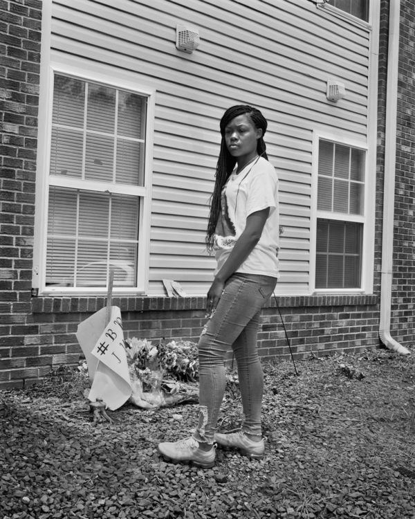 Photograph by LaToya Ruby Frazier. Breonna Taylor’s Sister, Juniyah Palmer, Standing Between the Two Front Bedroom Windows of the Apartment Where the Louisville Metro Police Department Fired Over 20 Bullets on March 13th, 2020, Just After 12:30 a.m. on Springfield Drive, Louisville, Kentucky.