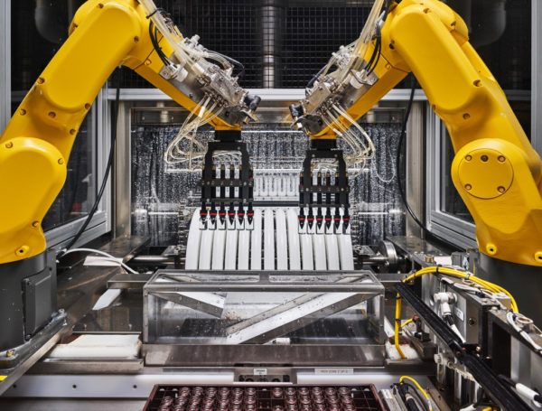 Photo: Christopher Payne/The New Yorker Caption: Robotic arms transfer the vials—twelve at a time—onto plastic tracks, which convey them through a chamber where they are further cleaned. Then they are air-dried and spray-coated. The facility is producing millions of vials a month.