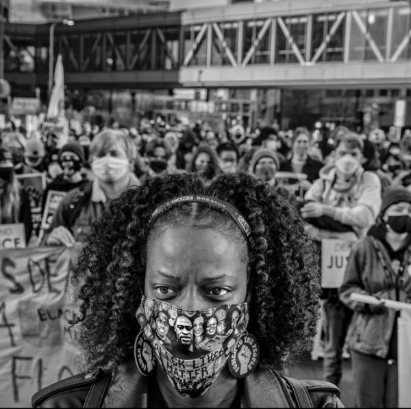 Woman, masked, stands in front of a crowd gathered for George Floyd's murder trial.