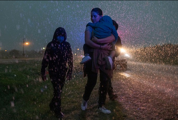 An asylum-seeking mother and her three children from Central America are followed by a Texas Highway Patrol officer as they look for cover during a heavy downfall, after crossing the Rio Grande river into the United States from Mexico, in La Joya, Texas, on May 19, 2021.