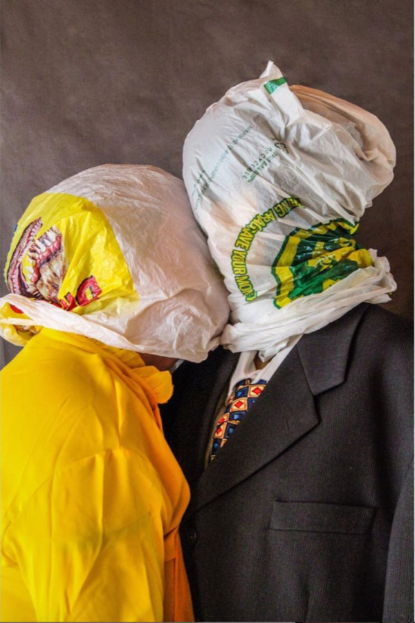 Two individuals with plastic bags over their heads kiss.